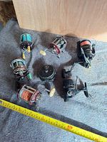 Six fishing reels arranged on fabric with measuring tape for scale