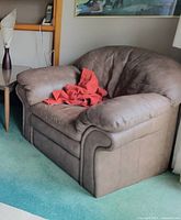 Front view of oversized brown leather armchair with red cloth on seat