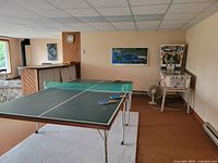 Full view of green folding ping pong table on metal legs with net, three paddles and one ball