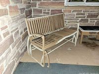 Full view of wood slat rocking bench against stone wall