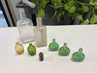 Group shot showing all bottles: two rectangular, one amber coin flask, five green coin flasks