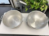 Top view of two aluminum colanders showing perforations and handles