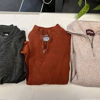Three folded sweaters displayed side-by-side