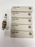 Five boxed BMW spark plugs with one displayed unboxed