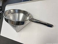 Overall view of stainless steel conical strainer lying on table