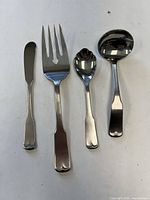 Four stainless steel utensils laid out: butter spreader, serving fork, serving spoon, ladle