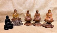 Group shot of all five Buddha figurines: amber resin on brass base, black resin with coin, three wood figures on lotus stands