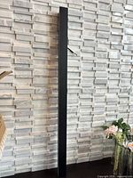 Full view of tall matte black bar wall sconce against tiled wall