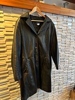 Front view of black leather coat on hanger showing buttons, collar and pockets