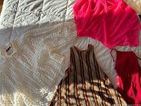 All four garments laid out on quilt: cream eyelet blouse, hot-pink chiffon blouse, multicolour striped top, red bodysuit