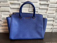 Front view of cobalt blue Michael Kors satchel bag showing logo, handles and color