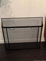 Full view of black metal fireplace screen showing mesh panels, handles and overall condition
