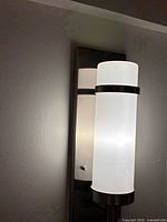 Sconce mounted showing brushed nickel backplate and frosted glass cylinder