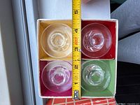 Top view of four clear glass votive holders in original box, tape measure showing width