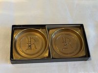 Top view of two brass coasters seated in original box