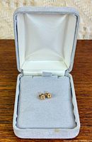 Open grey velvet-lined jewellery box showing pair of gold ball earrings