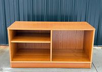 Front view of teak media cabinet showing two open bays and plinth base