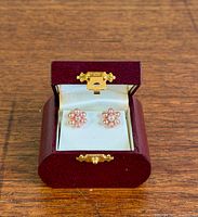 Earrings displayed in open burgundy jewelry box on wood surface