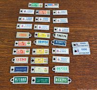 Full group of 27 Alberta miniature license plate keychain tags on wood surface