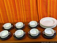 Six bowls each on black saucer beside stack of plates