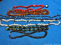 All seven gemstone bead necklaces laid out on blue background