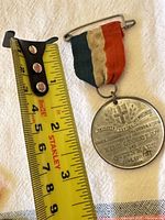 Front view of medal showing design, ribbon, and tape measure for scale