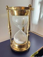 Full view of brass-framed hourglass showing glass timer with white sand