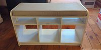 Overall view of white cubby bench with beige cushion showing six compartments and visible wear on edges