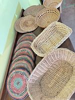 Group of wicker baskets and braided mats on wooden surface