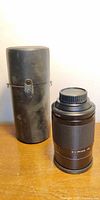 Lens standing beside cylindrical hard case, caps fitted