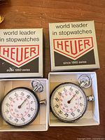 Pair of Heuer stopwatches in open boxes beside closed lids