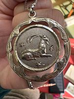 Front of sterling silver Capricorn medallion pendant showing raised goat motif, openwork border and attached chain