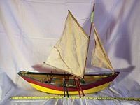 Full view of painted wooden sailboat model with sails and oars, measuring tape below
