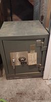 Front view of olive-green Sears safe showing dial, handle, brass plate, taped combination sheet