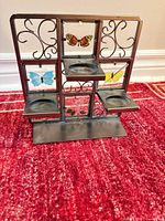 Front view of metal candle holder showing three tiers, scrollwork, colored butterfly glass panels, and candle cup recesses