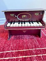 Front view of burgundy toy piano showing keyboard and gold trim