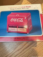 Front of box showing image of Coca-Cola musical bank and product details