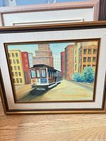 Front view of framed painting showing city street and cable car scene