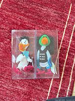 Both Infamous Meanies plush ducks side by side in plastic cases