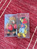 Both plush toys in their display boxes on red background