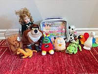 Group shot of all 11 items including porcelain doll, plush toys, zipped case