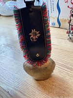 Front view of brass cowbell with leather strap and colourful fringe