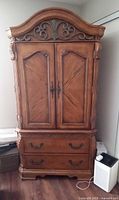 Front view of solid oak armoire showing arched top, carved scrollwork, double doors, two drawers