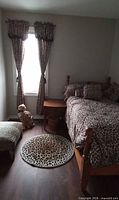 Full view of bed with bedding, curtains, rug, ottoman and plush leopard