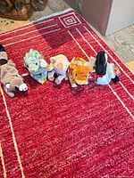 Five plush animals lined up on red rug