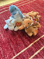 Three Ty Beanie Baby plush animals (dolphin, unicorn, fox) grouped on red rug
