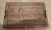Top view of wooden cutting board showing metal handles, juice groove and carved pattern