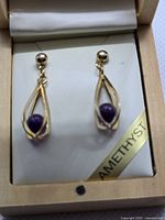 Close view of earrings in box showing teardrop frames and amethyst beads