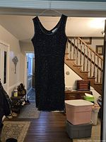 Full view of black beaded sleeveless dress hanging, showing overall style and length
