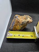 Side view of boulder opal next to tape measure showing roughly 3 inch length